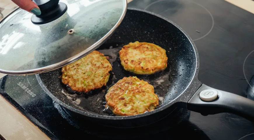 Decken Sie die Bratpfanne mit Zucchini-Pfannkuchen mit einem Deckel ab