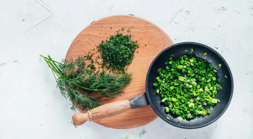 Für Zucchini-Pfannkuchen den Dill schneiden und die Frühlingszwiebeln anbraten